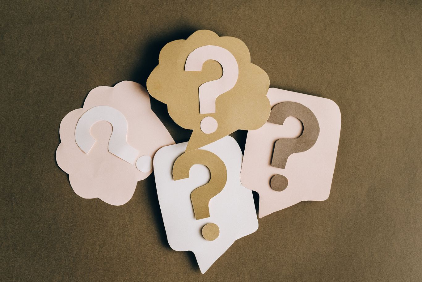 picture of a light brown background with different shaped speech bubbles cut out of different shades of light brown and cream card. Each bubble has a question mark in it, also cut out of different shades of brown and cream card